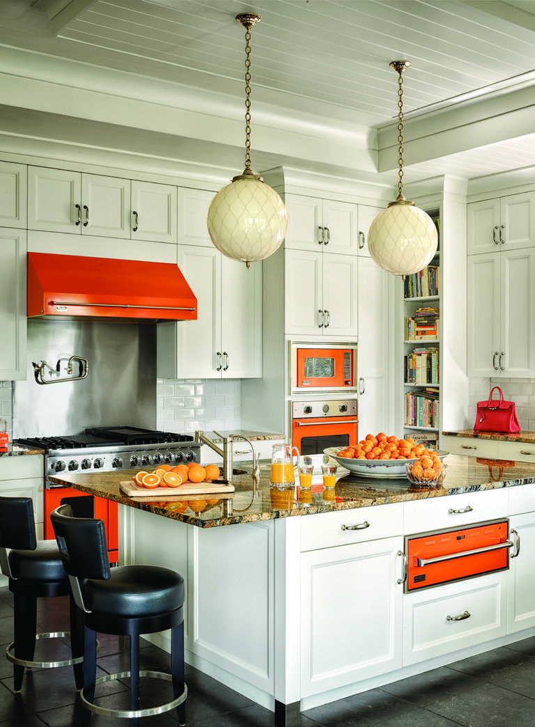 Orange stove, vent hood, and wall ovens contrast with a white kitchen 