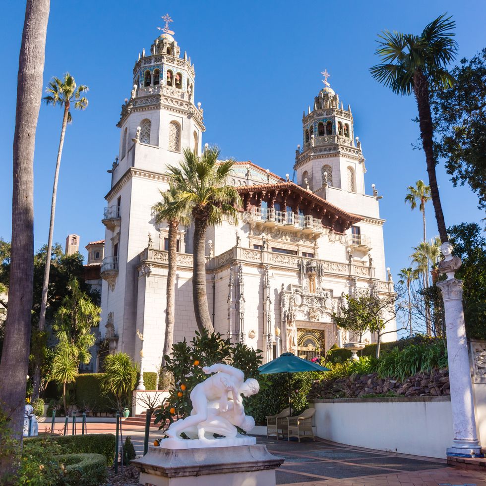 hearst castle from the front showing full facade, towers, palm trees, sun, clear blue sky