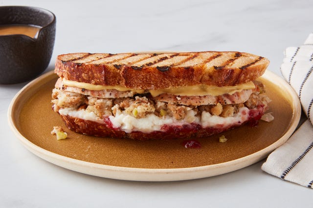 a grilled sandwich with turkey stuffing and cranberry sauce on a plate beside a cup of coffee