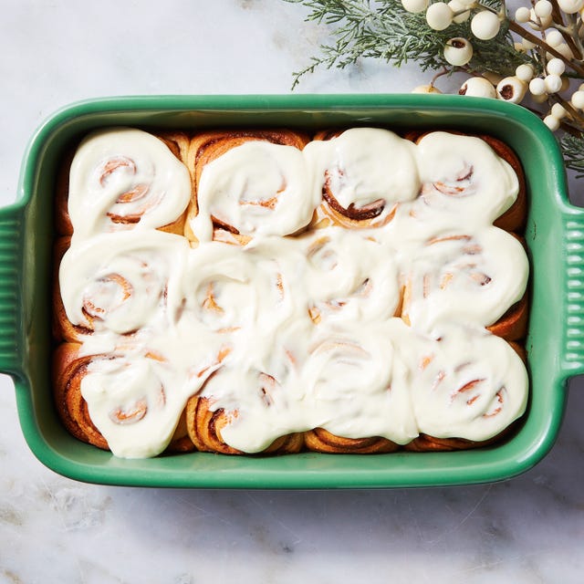 baked cinnamon rolls topped with cream cheese frosting in a green baking dish