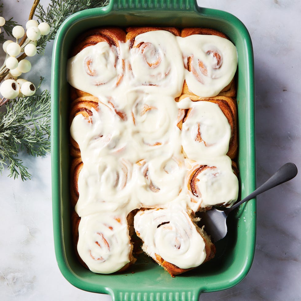 freshly baked cinnamon rolls topped with cream cheese frosting in a green baking dish