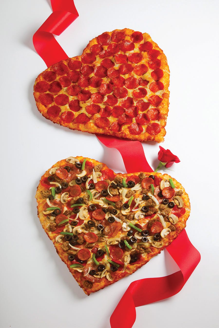 two heartshaped pizzas garnished with toppings surrounded by a red ribbon