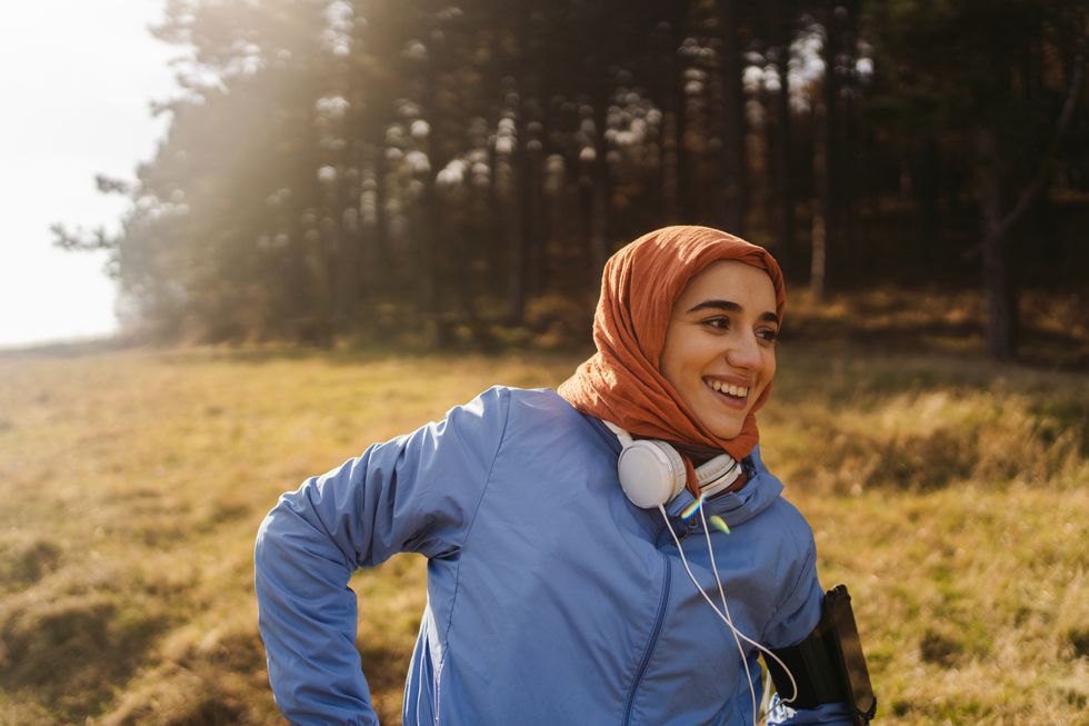 young woman with a hijab smiles as she runs outdoors