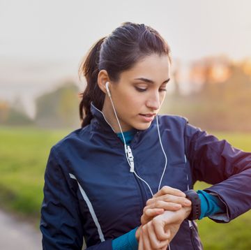young athlete listening to music during workout at park and adjusting smart watch