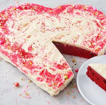 heart shaped red velvet cake covered in icing and sprinkles with a slice taken out of it on a plate