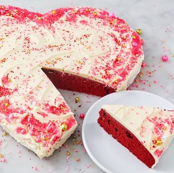 heart shaped red velvet cake covered in icing and sprinkles with a slice taken out of it on a plate