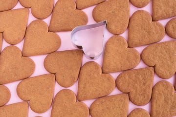 heart shaped gingerbread cookies cinnamon with heart shaped dought cutter againt pink background with copy space love and romanticism concept