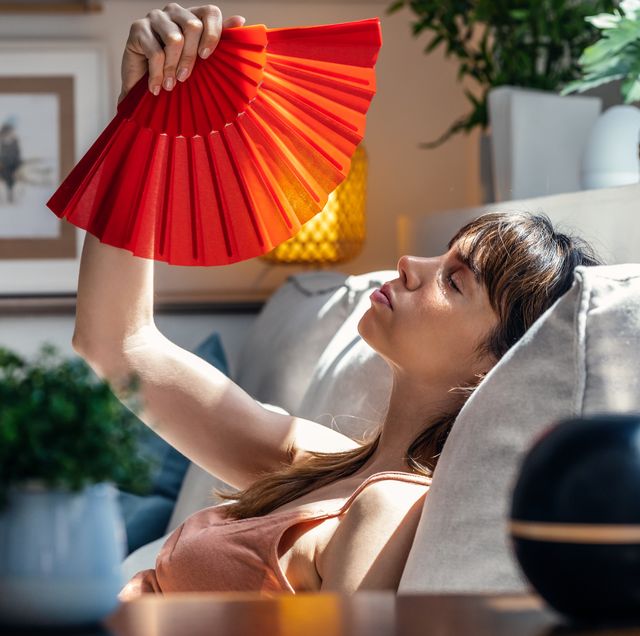 young woman fanning herself while sitting on couch at home