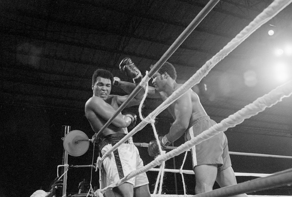 george foreman punching muhammad ali up against the ropes of a boxing ring