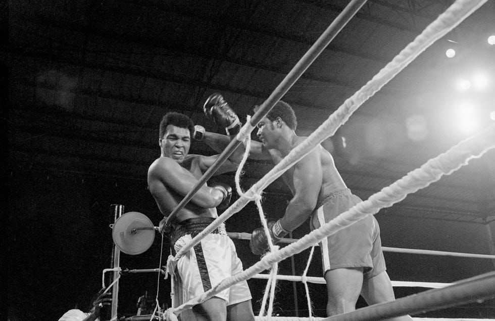 george foreman punching muhammad ali up against the ropes of a boxing ring