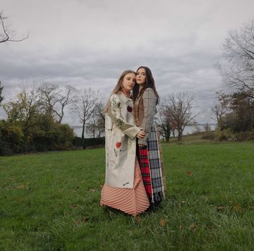 two sisters stand in a grassy field with a body of water in the background