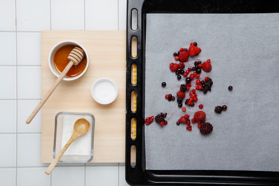 frutos rojos en una bandeja de horno junto a un cuenco con miel y azúcar