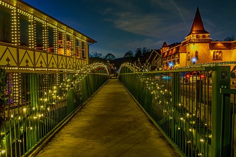 bridge with white lights on beside alpine villagelooking buildings lines in white light