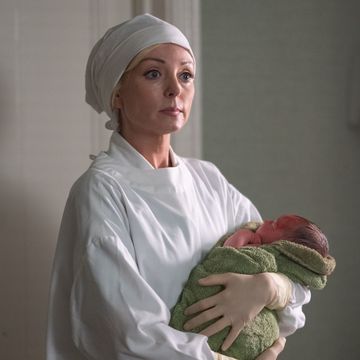 helen george as nurse trixie franklin in a surgical cap and gown holding a newborn baby, call the midwife, season 13