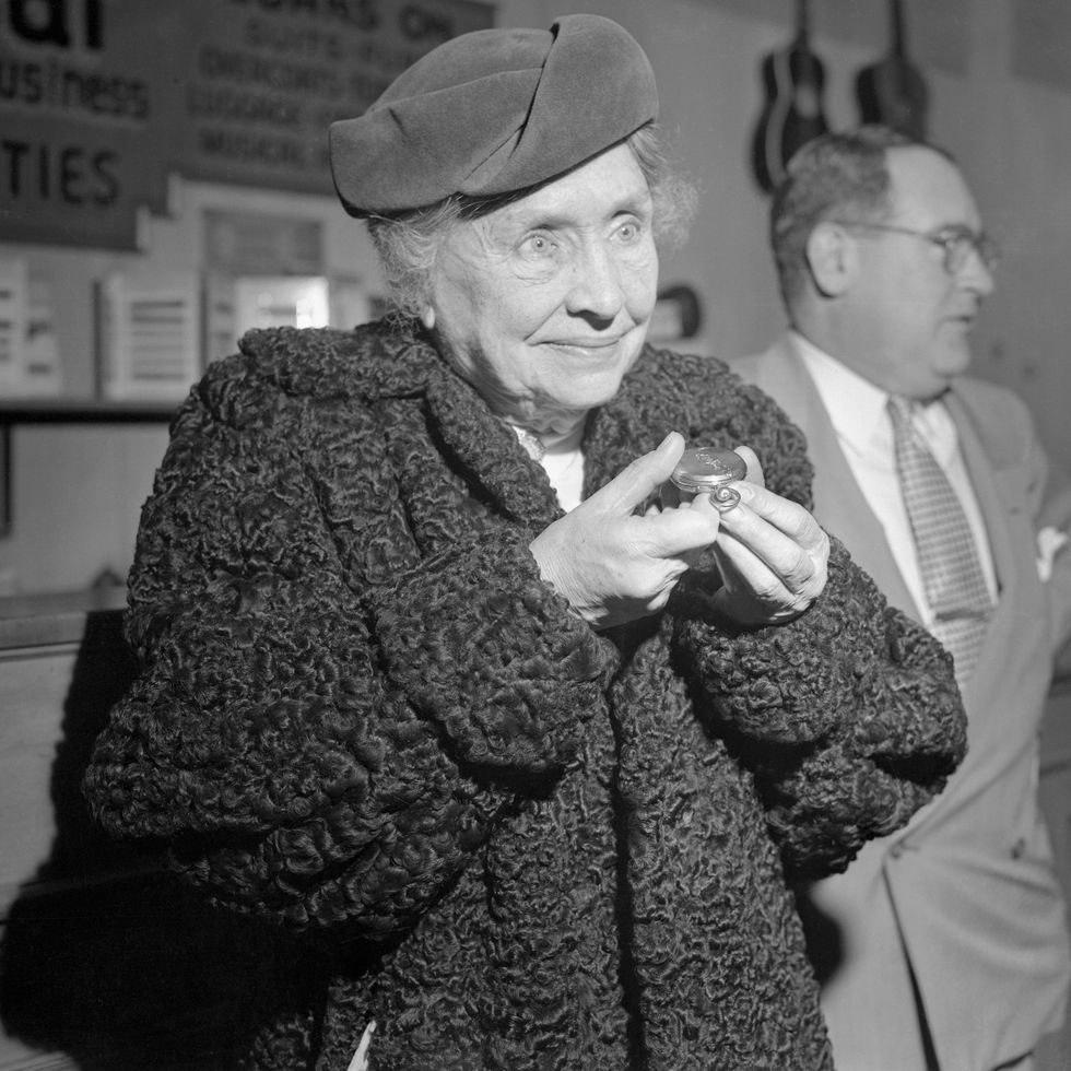 helen keller holds a pocket watch and wears a fuzzy coat and hat