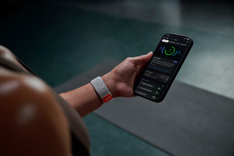 a hand holding a smartphone displaying fitness data and statistics accompanied by a wearable fitness tracker on the wrist