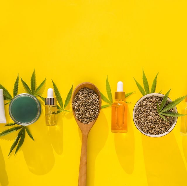 hemp cosmetic products glass bottles with oil, hemp seed extract, cream and hemp seeds and leaves on a yellow background