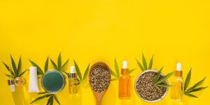 hemp cosmetic products glass bottles with oil, hemp seed extract, cream and hemp seeds and leaves on a yellow background