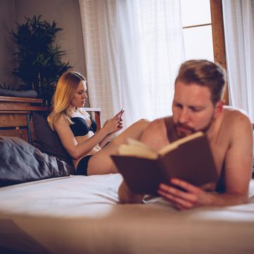 pareja en la cama, ella aburrida y él con un libro