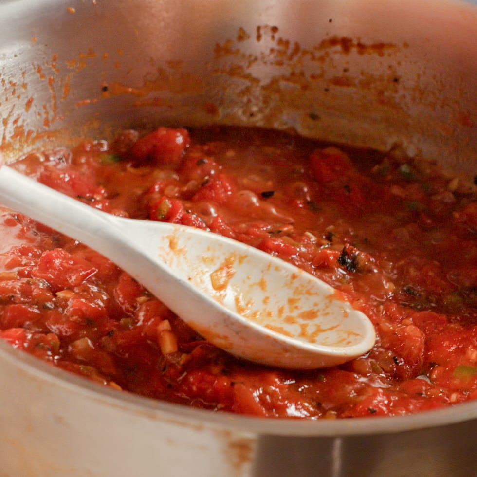 smashing down on tomatoes in a skillet with a spoon