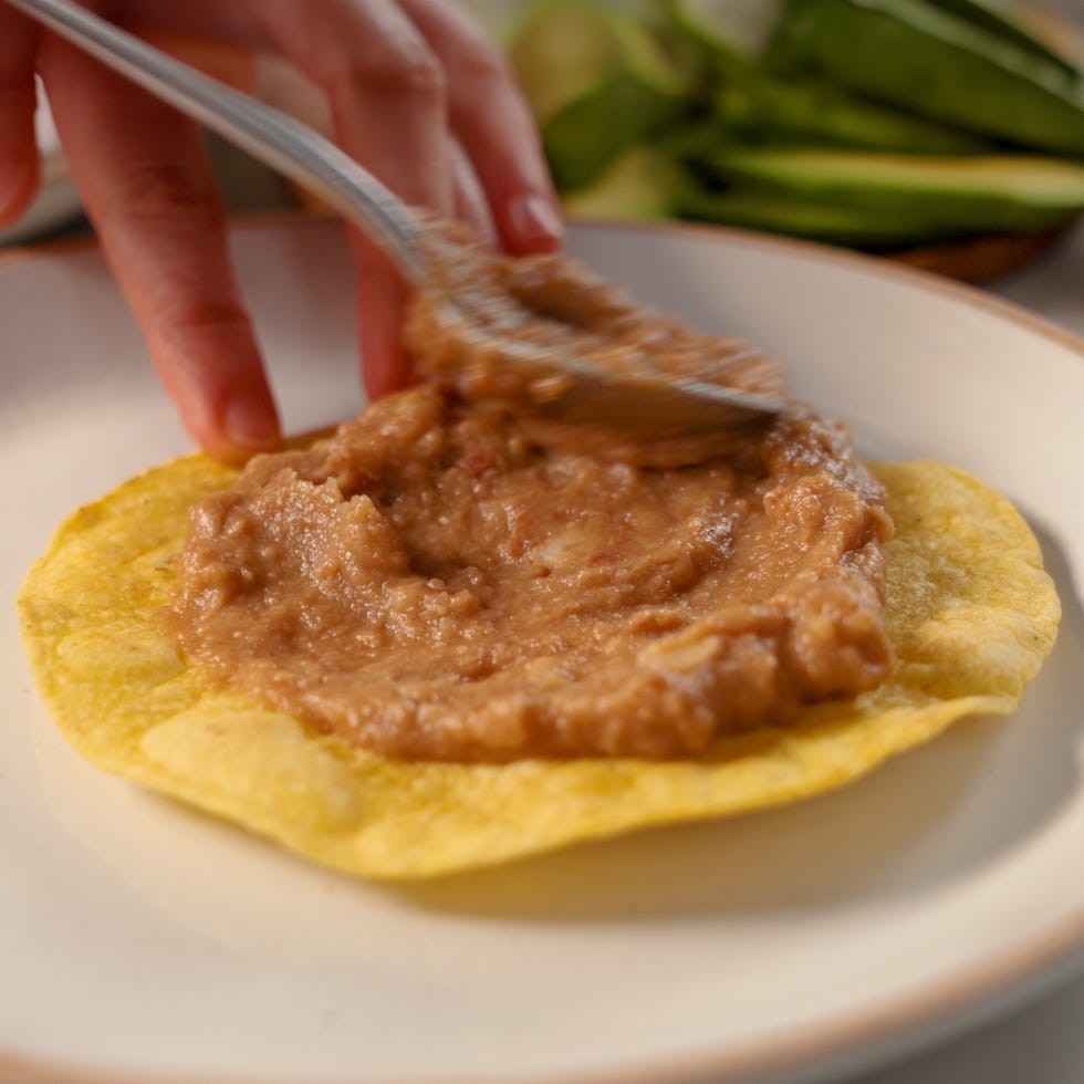 spooning refried beans over a tortilla