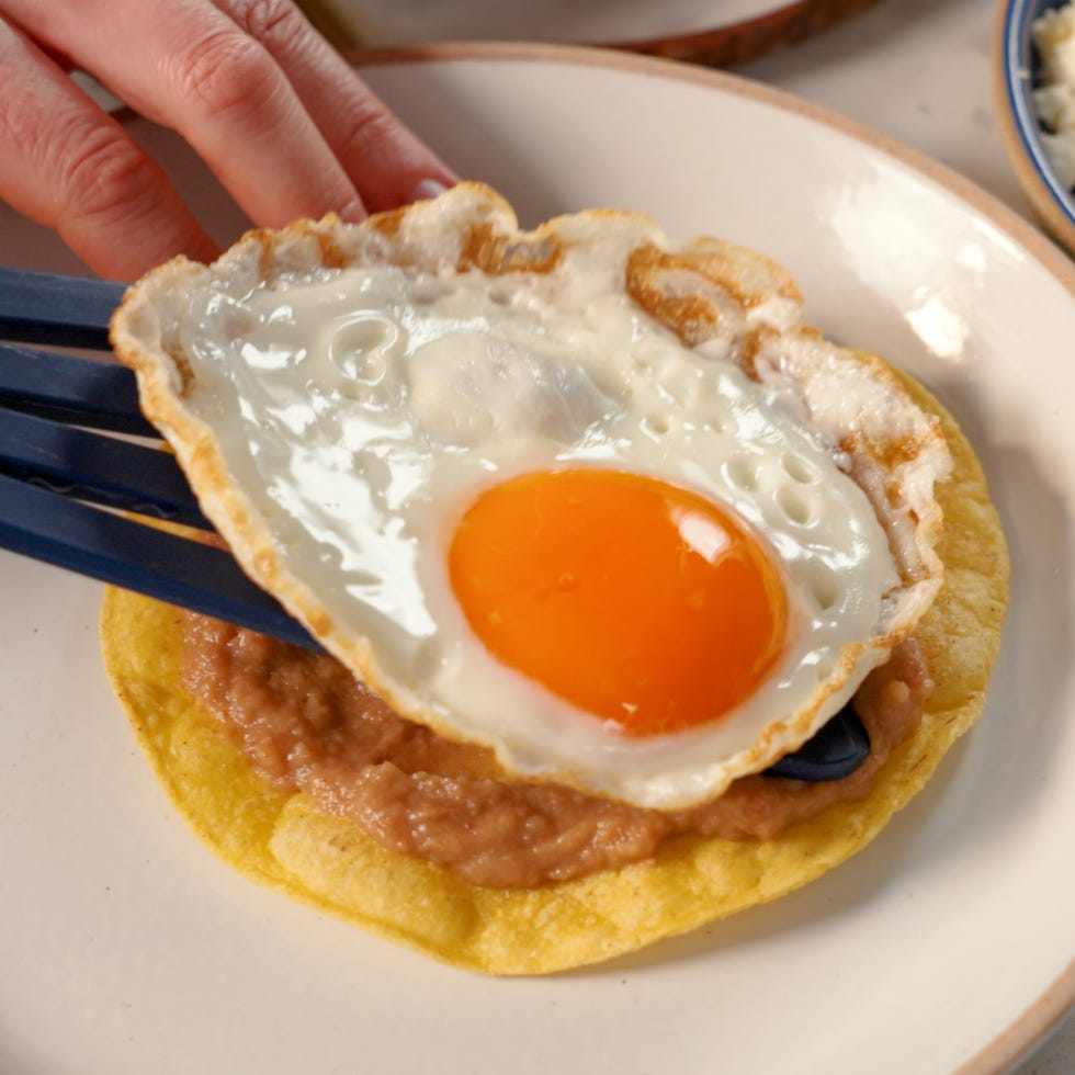 a fried egg being placed on a tortilla with refried beans