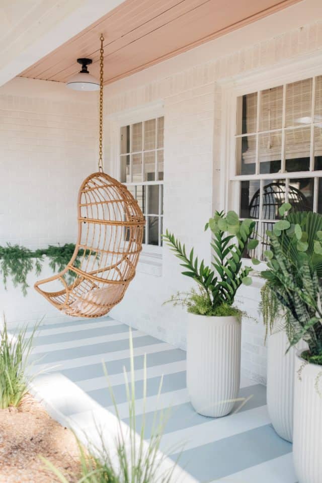 hanging rattan chair on a porch with potted plants beside windows
