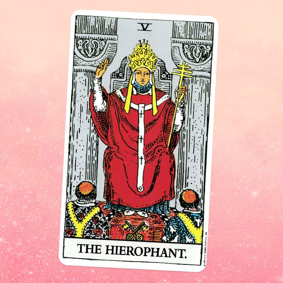 the tarot card the hierophant, showing a person in a red robe and gold crown sits on a throne, with two people kneeling in front of them
