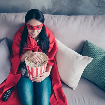 high angle top above photo beautiful she her superpower lady costume hold popcorn container watch premiere new long wait comics picture wear red eye mask mantle sit sofa couch divan house indoors