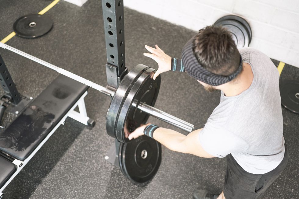 high angle view of a man in sportswear standing preparing the weights discs on the bar inside the gym