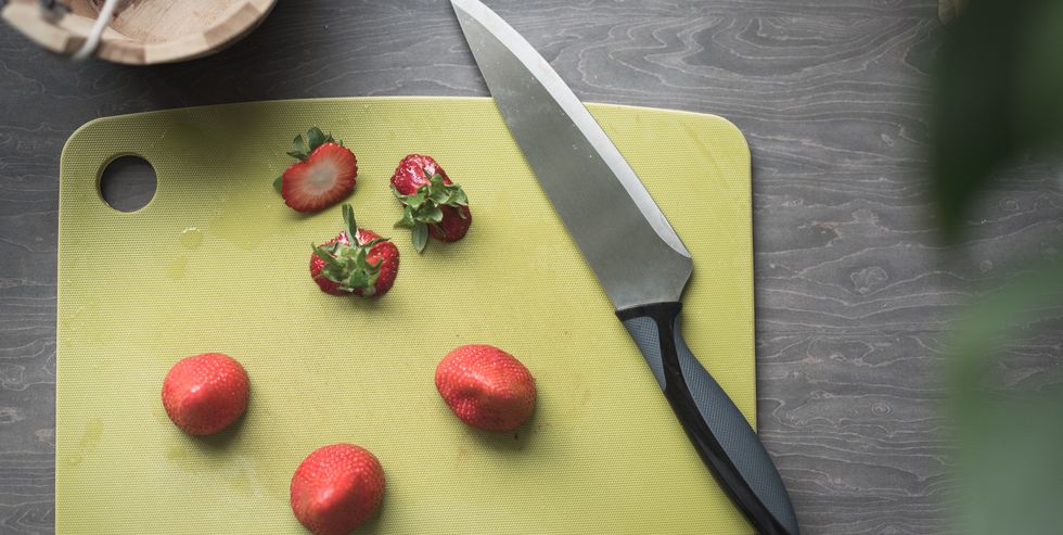 high angle view of a set of freshly cut strawberries, a green chopping board, a big knife and a wooden bucket on a kitchen top