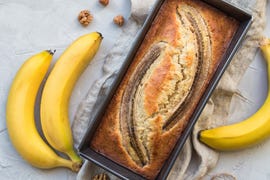 bananenbrood in bakvorm op tafel, met bananen ernaast