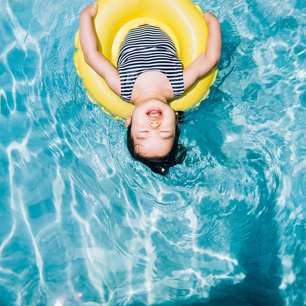 high angle view of cute asian toddler girl closed her eyes while floating with an inflatable ring relaxing at swimming pool