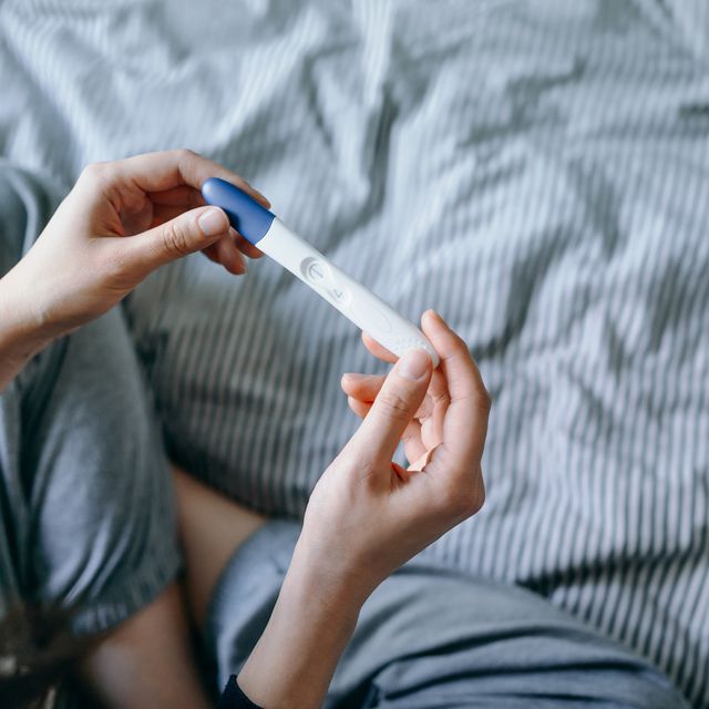 high angle view of disappointed young asian woman sitting on the bed and holding a negative pregnancy test life events, infertility and family concept