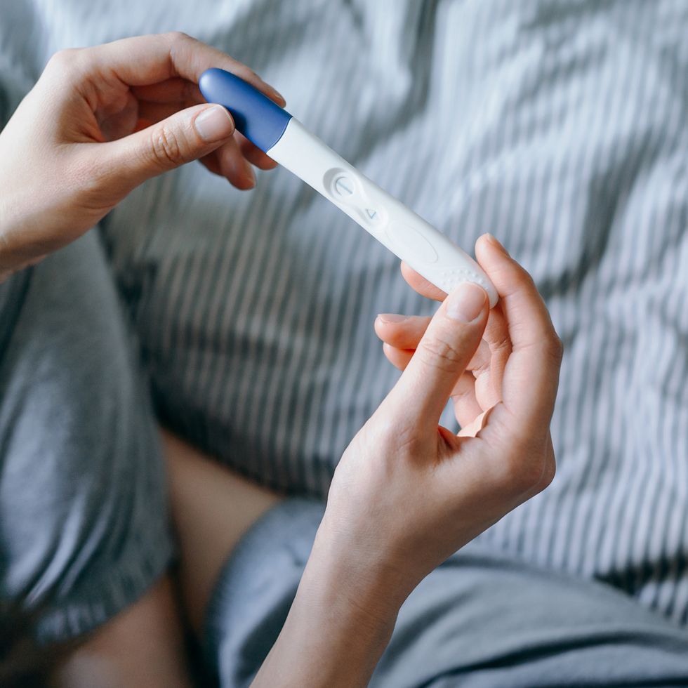 high angle view of disappointed young asian woman sitting on the bed and holding a negative pregnancy test life events, infertility and family concept
