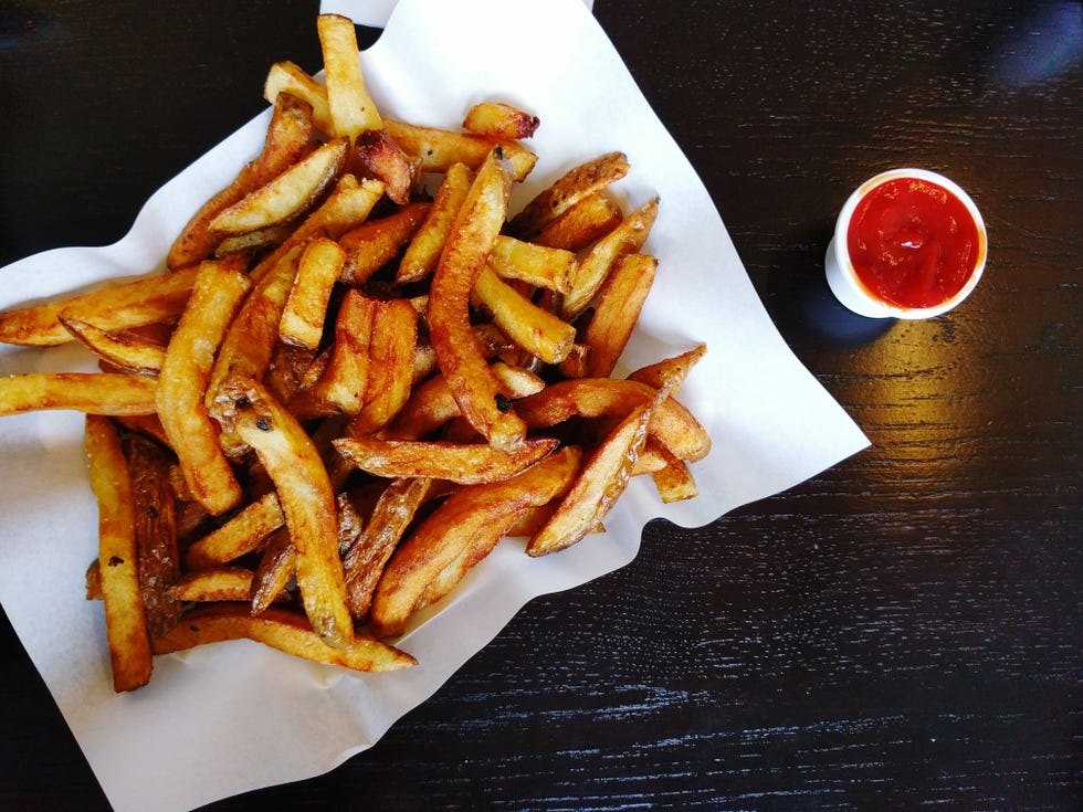 High Angle View Of French Fries In Wax Paper By Sauce On Table