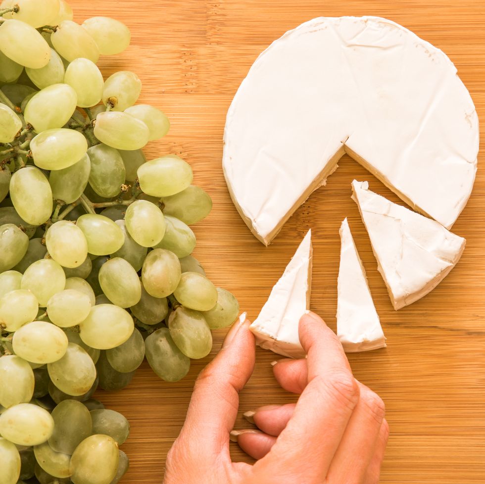 high angle view of hand holding a piece of brie cheese on table