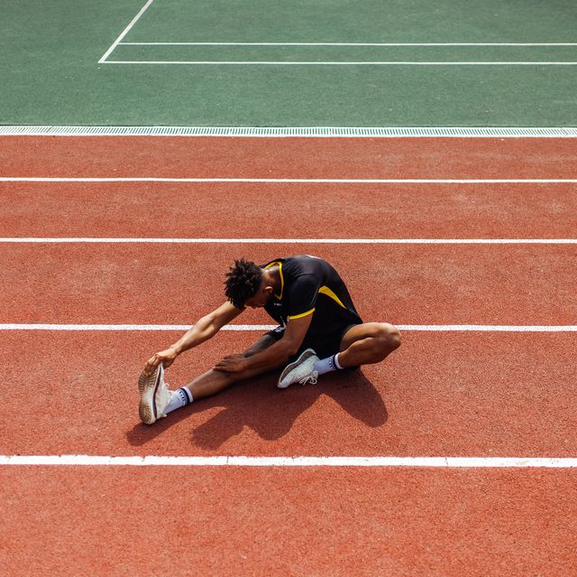 high angle view of male sports person in soccer uniform doing stretching exercises sitting on running track