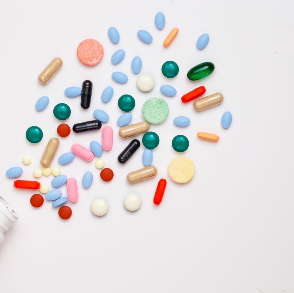 High Angle View Of Multi Colored Pills And Bottle Against White Background