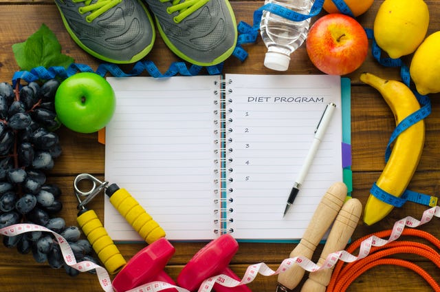 high angle view of open book amidst fruits and exercise equipment on table