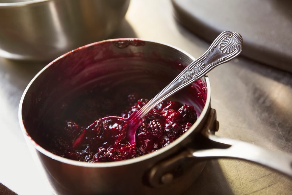 High angle view of red berry compote in a metal saucepan with a silver spoon.