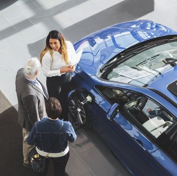 high angle view of saleswoman showing car to customers at showroom