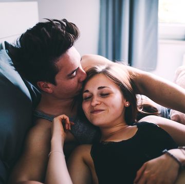 High Angle View Of Smiling Young Man Kissing Woman Sleeping On Bed At Home
