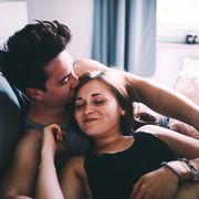 High Angle View Of Smiling Young Man Kissing Woman Sleeping On Bed At Home