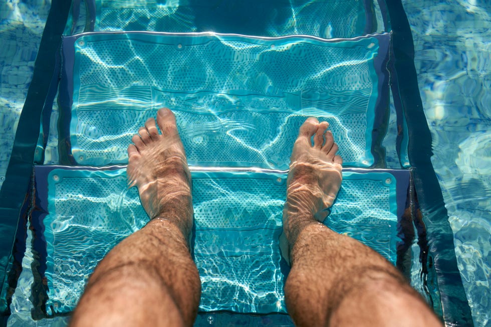 high angle view of the feet of a man standing on the stairs of a swimming pool