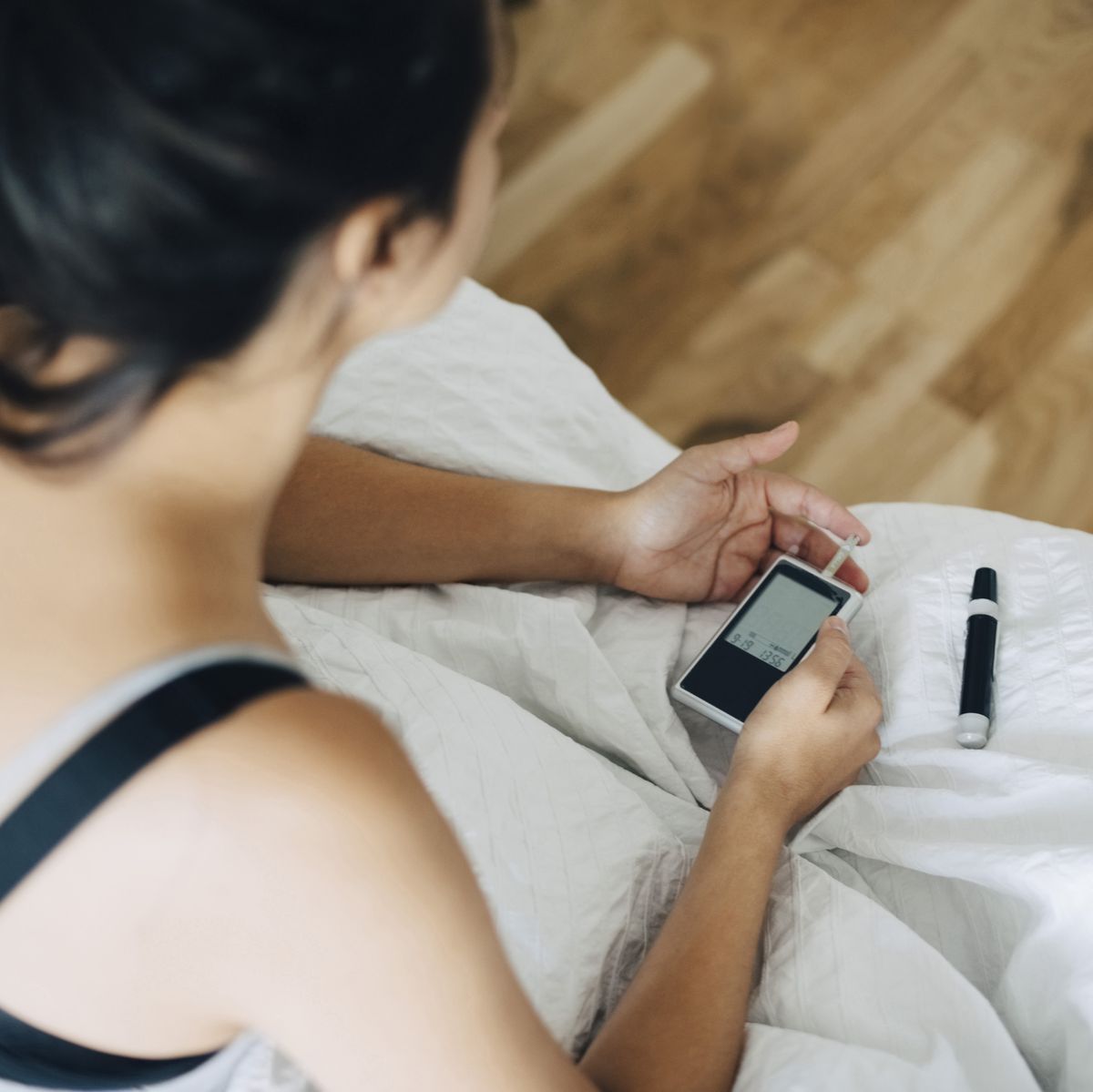 High angle view of woman checking blood sugar level while sitting on bed