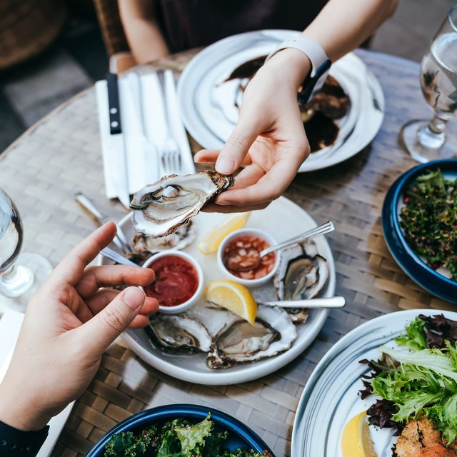 high angle view of woman passing fresh oyster to man across the dining table during lunch, enjoying a scrumptious meal in outdoor restaurant sharing and togetherness eating out lifestyle outdoor dining concept