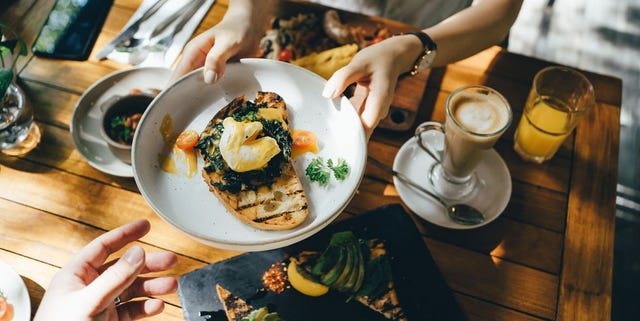 high angle view of woman passing platter of food to friend during brunch in an outdoor restaurant against beautiful sunlight