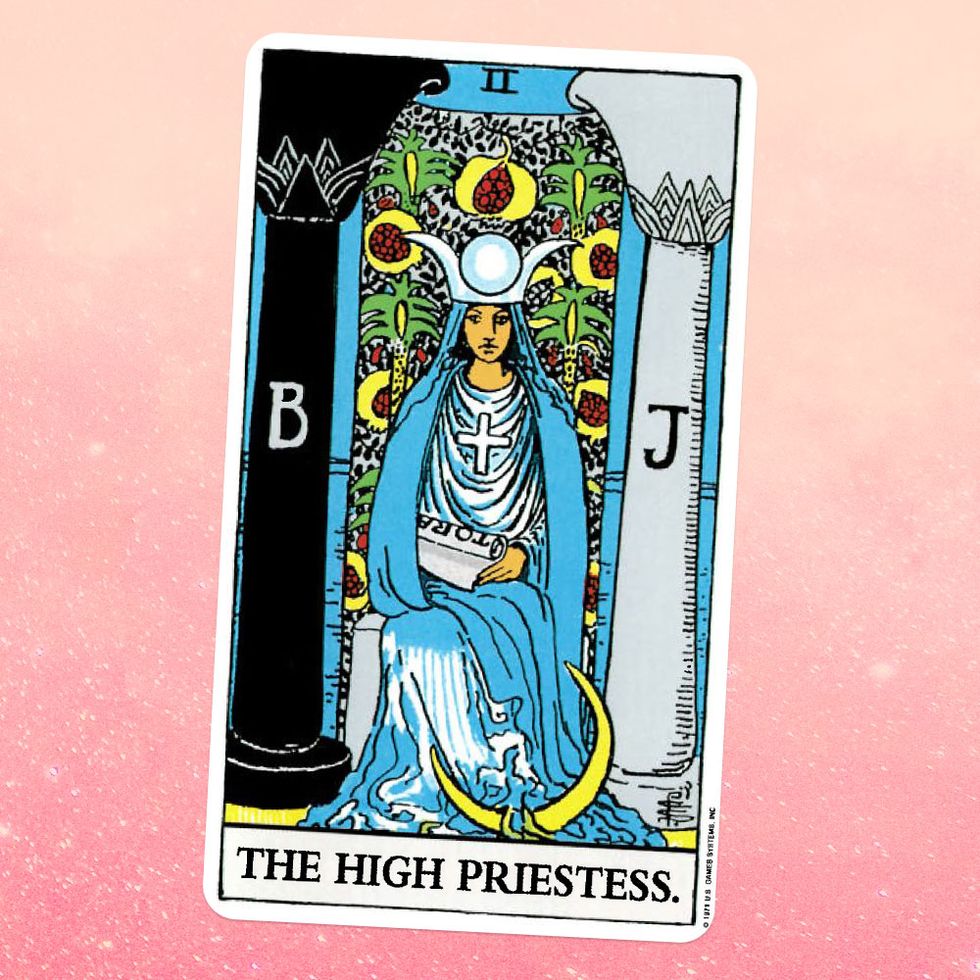 the high priestess tarot card, showing a woman in a giant blue robe and matching hat sitting between two pillars