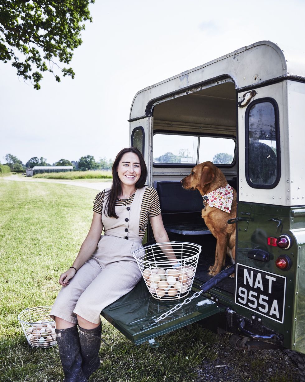 amelia strong wearing wellies leaning on the open boot of her landrover with her labrador and baskets of eggs